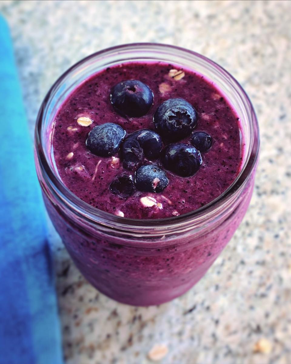 Overhead view of a thick, vibrant purple Blueberry Oat Breakfast Smoothie in a glass jar, topped with fresh blueberries and oats.