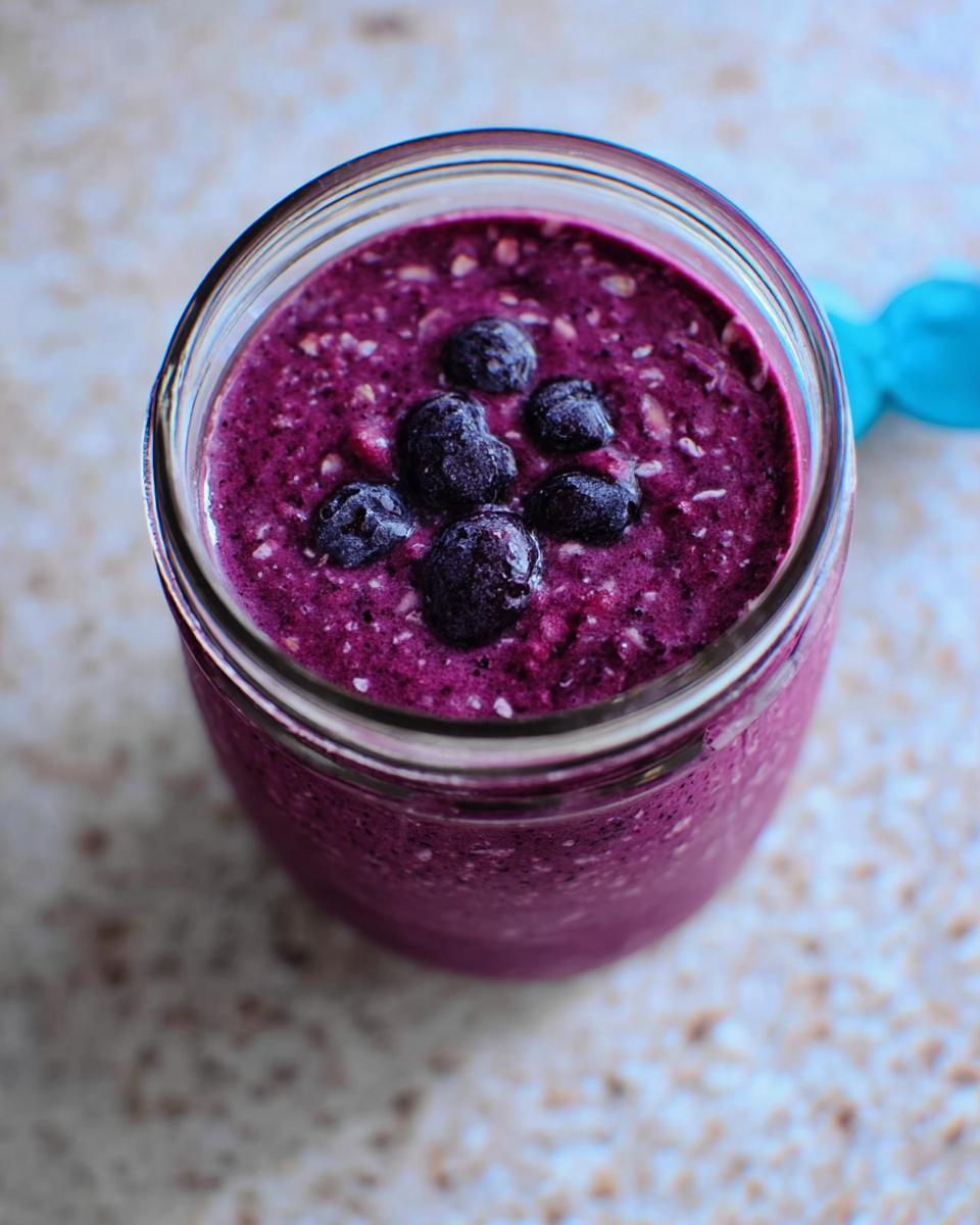 Overhead view of a thick Blueberry Oat Breakfast Smoothie topped with whole blueberries in a glass jar.