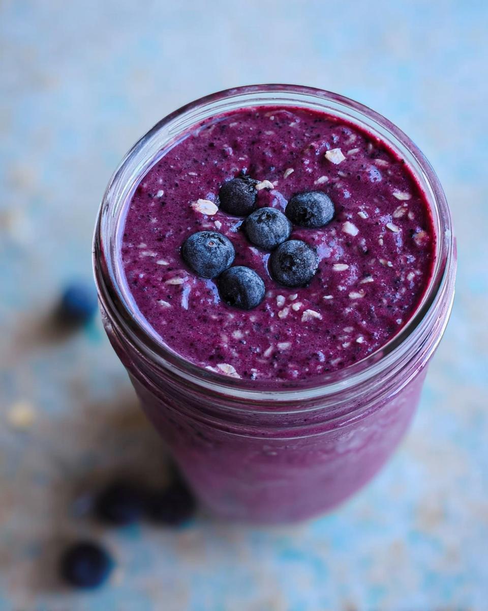 Overhead view of a thick Blueberry Oat Breakfast Smoothie topped with fresh blueberries and visible oat flakes.