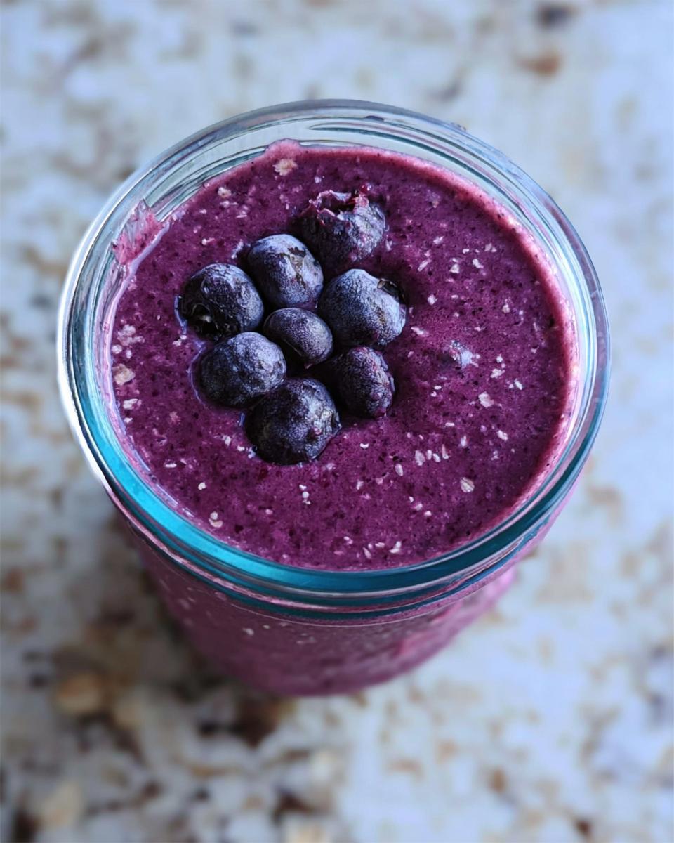 Overhead view of a vibrant purple Blueberry Oat Breakfast Smoothie topped with frozen blueberries.