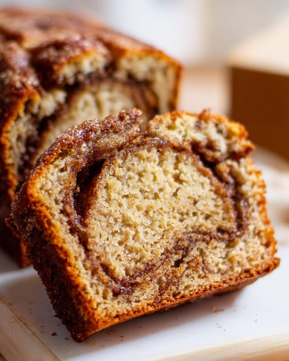 A thick slice of moist Cinnamon Swirl Banana Bread showing a rich cinnamon swirl inside and a sugary crust.