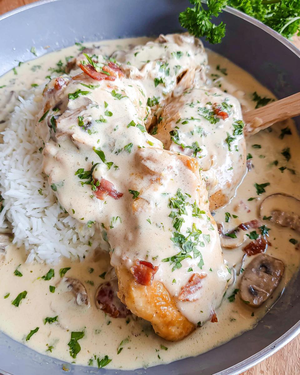 Close-up of Creamy Smothered Chicken and Rice Recipe served in a skillet with mushrooms and bacon.