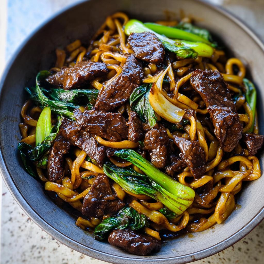 A close-up of a bowl filled with tender beef strips, bok choy, and thick noodles in a savory sauce, perfect for easy dinner recipes.