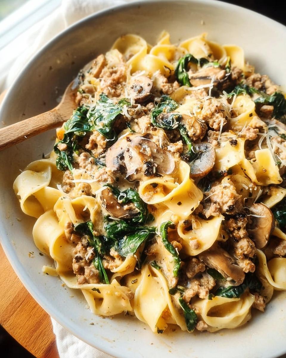 A close-up of a creamy skillet pasta with sausage, spinach, and mushrooms, perfect for easy dinner recipes.