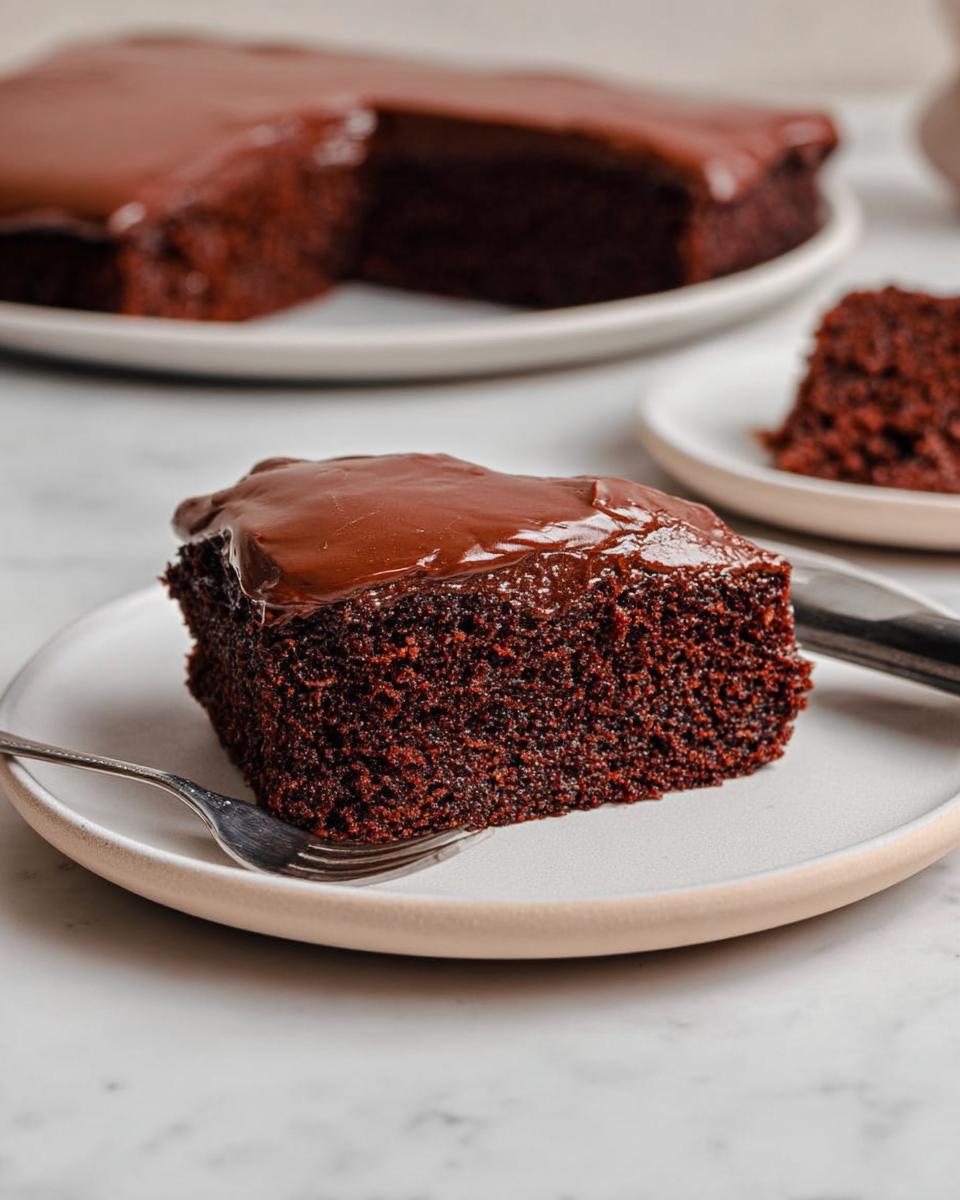 Close-up of a moist slice of Easy Snacking Sheet Cake topped with glossy chocolate frosting, served on a plate.
