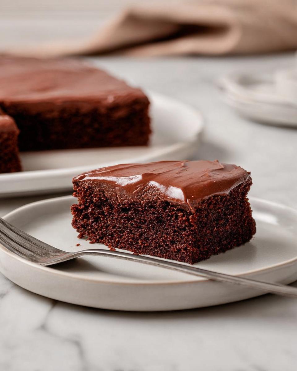 A square slice of rich, dark chocolate Easy Snacking Sheet Cake topped with glossy frosting on a plate.