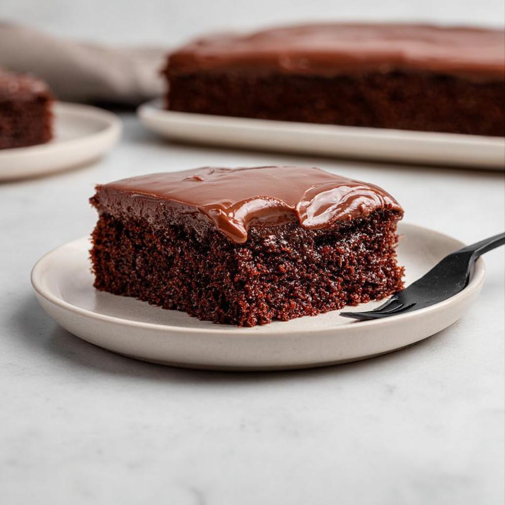 A moist slice of Easy Snacking Sheet Cake topped with glossy chocolate frosting on a small plate.