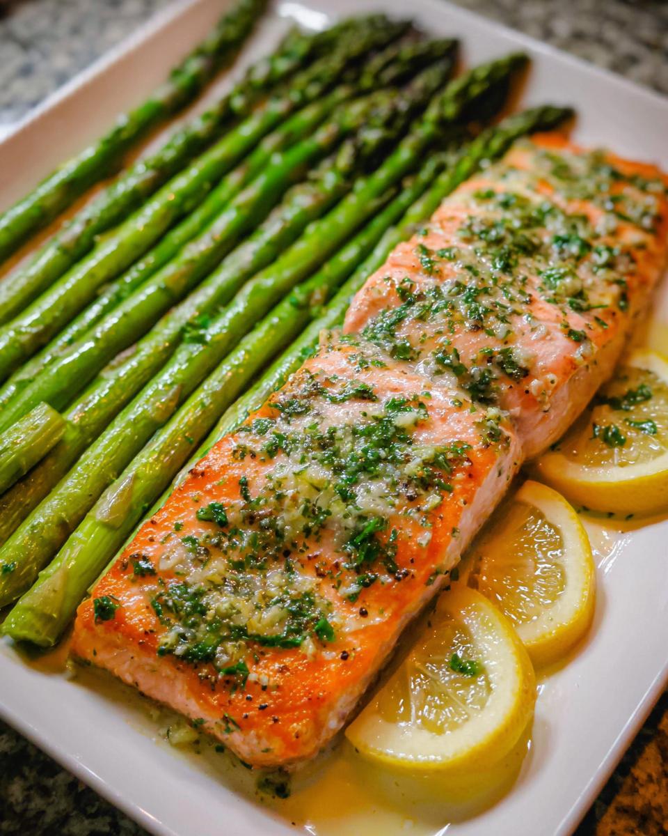 A cooked fillet of Garlic Butter Salmon & Asparagus served on a white platter with lemon slices.