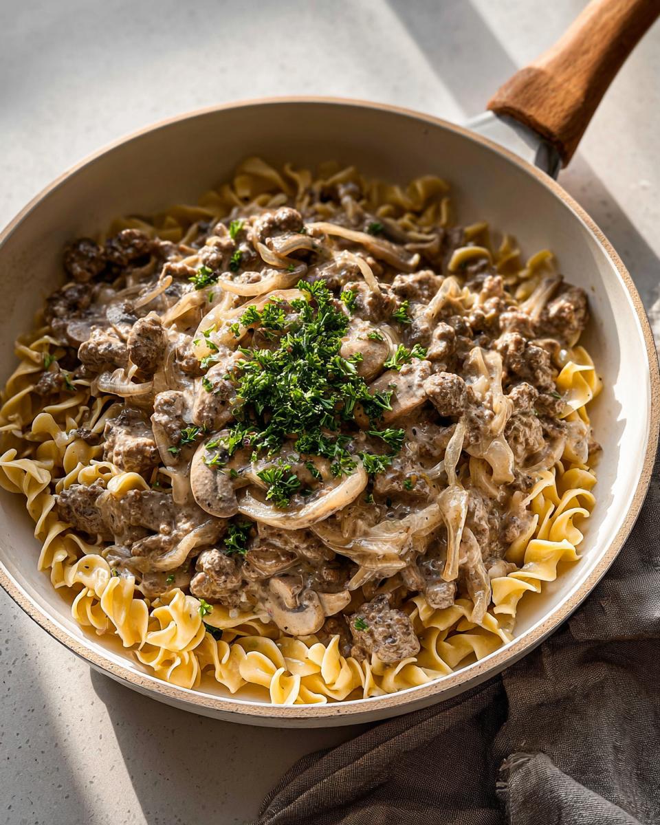 A skillet filled with creamy Ground Beef Stroganoff served over egg noodles and topped with fresh parsley.
