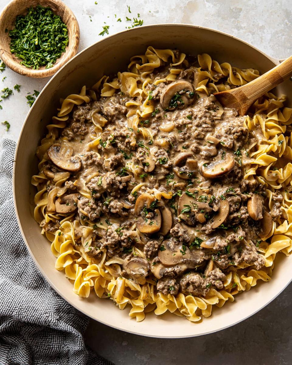 A large skillet filled with creamy Ground Beef Stroganoff mixed with sliced mushrooms and served over wide egg noodles.