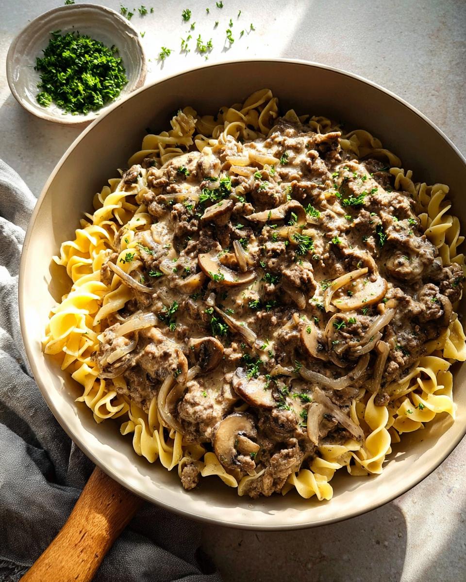 A skillet filled with creamy Ground Beef Stroganoff served over wide egg noodles, garnished with parsley.
