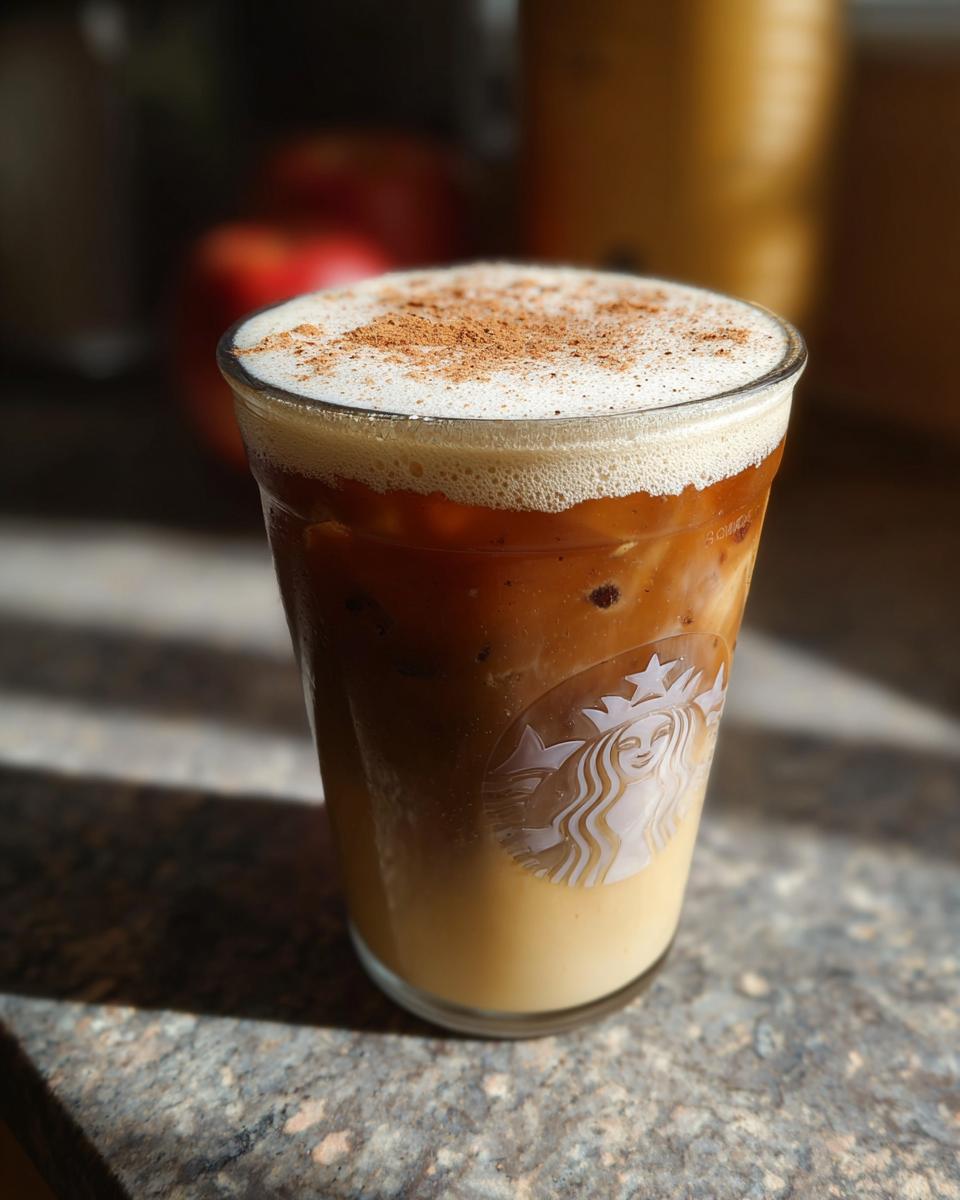 A close-up of an iced coffee Starbucks drink with foamed milk and cinnamon sprinkled on top.