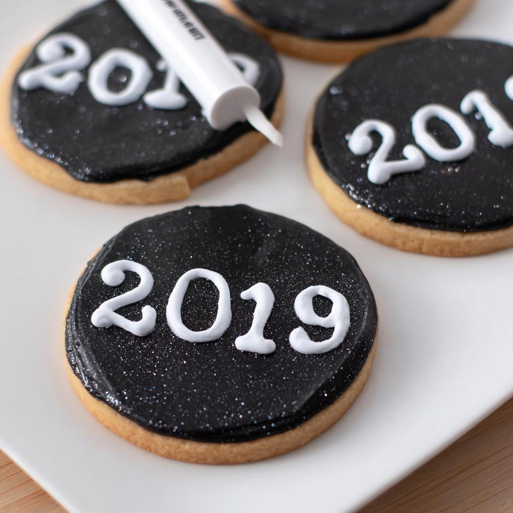 Close-up of round sugar cookies decorated for New Year’s Eve with black sparkly icing and white '2019' piped on top.