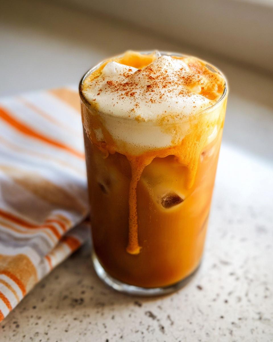 A tall glass filled with iced Pumpkin Cream Cold Brew (Copycat), topped with thick foam and pumpkin spice.