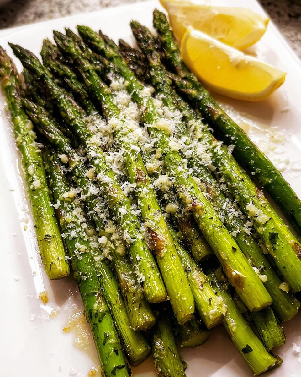 A close-up of bright green Roasted Asparagus with Parmesan cheese sprinkled on top, served with lemon wedges.