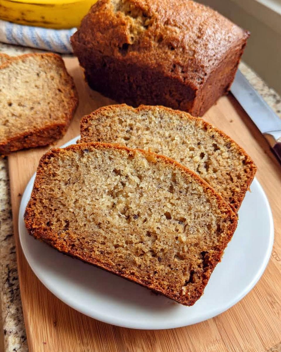 Slices of moist One Bowl Banana Bread served on a white plate next to the full loaf.