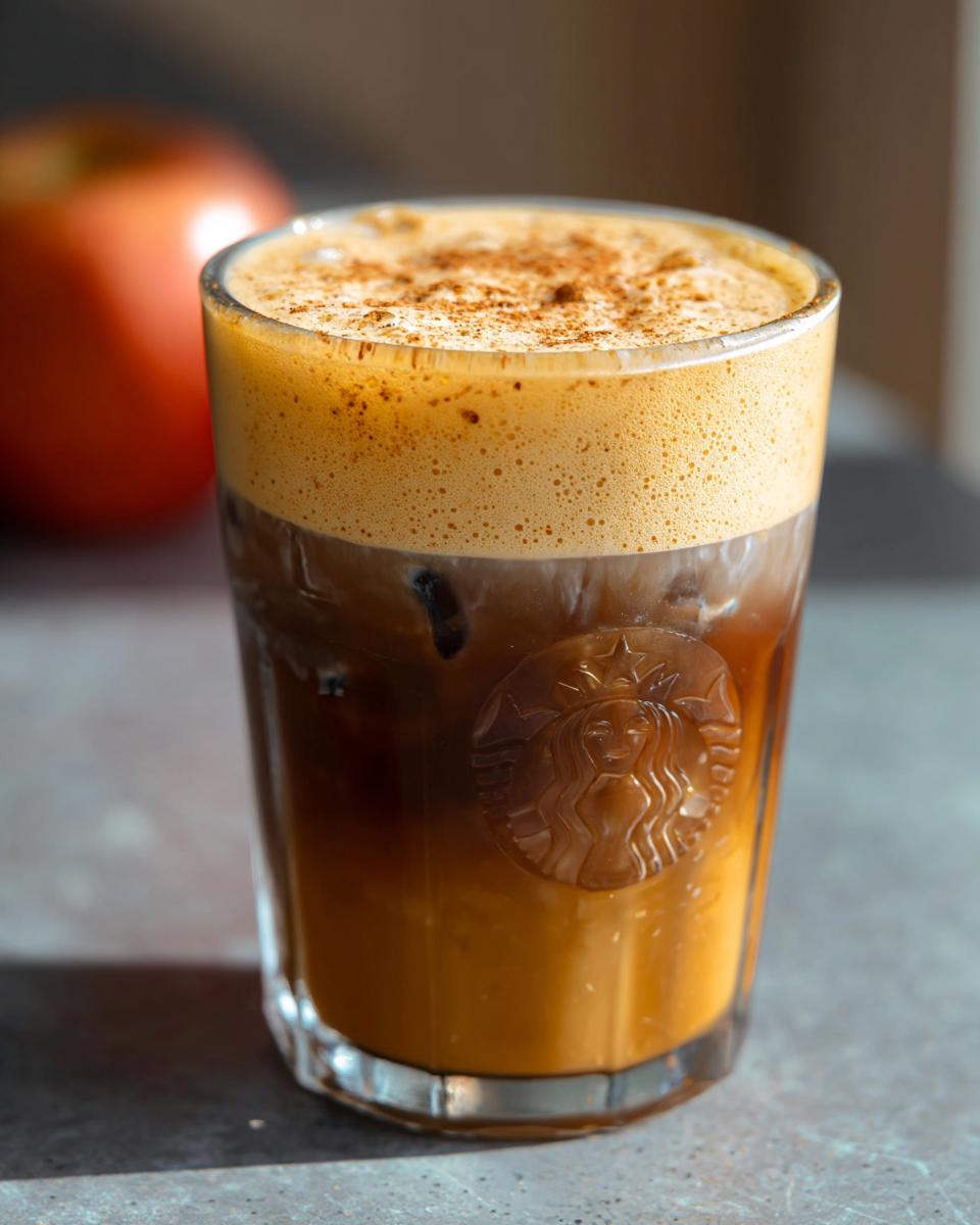 A refreshing iced coffee drink with foamy milk and cinnamon topping, in a Starbucks branded glass.