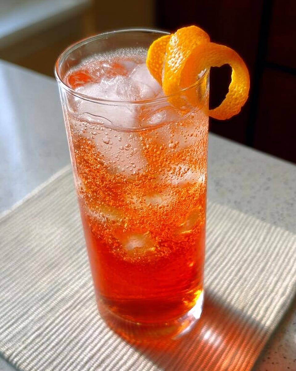 Close-up of a tall glass filled with ice and a vibrant orange Thanksgiving drink, garnished with a twisted orange peel.