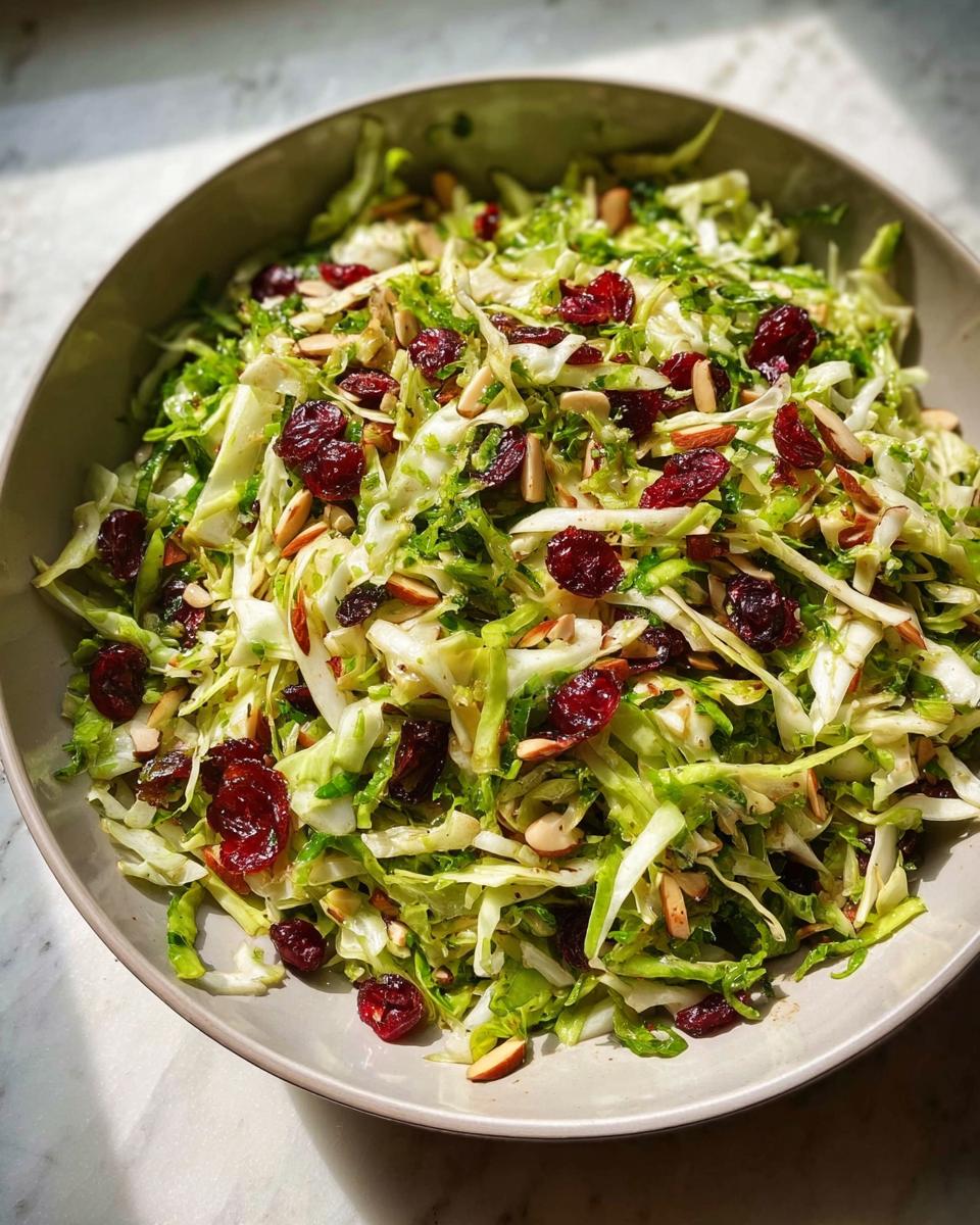 A vibrant Thanksgiving salad featuring shredded Brussels sprouts, dried cranberries, and slivered almonds in a large bowl.