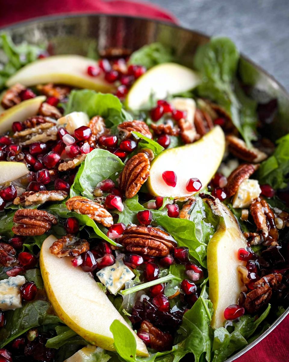Close-up of a Thanksgiving salad recipe with fresh greens, pear slices, pomegranate seeds, pecans, and blue cheese.