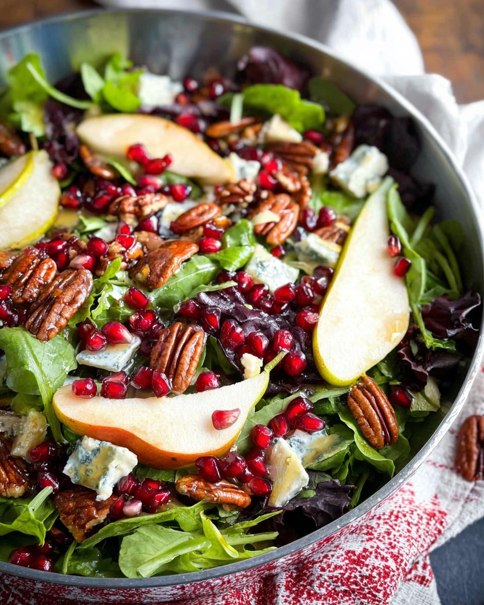 A festive Thanksgiving salad recipe featuring fresh greens, sliced pears, pomegranate seeds, pecans, and blue cheese.