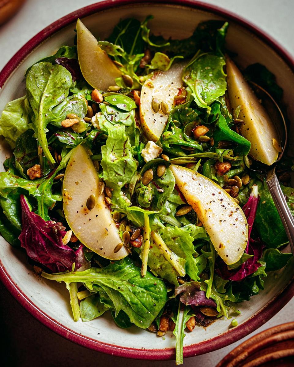 A vibrant Thanksgiving salad recipe featuring fresh greens, sliced pears, pumpkin seeds, and nuts in a bowl.