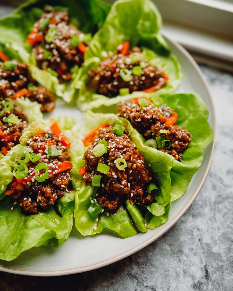 Close-up of several Asian Ground Beef Lettuce Wraps served on a white plate, topped with sesame seeds and scallions.