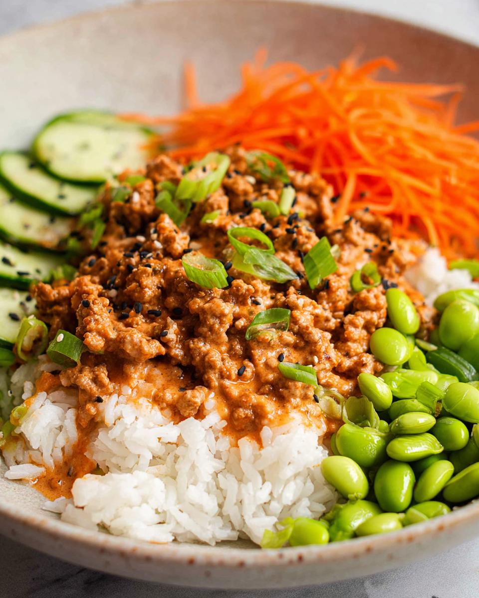 A close-up of Bang Bang Ground Turkey Rice Bowls featuring creamy ground turkey over white rice, topped with edamame, shredded carrots, and cucumbers.