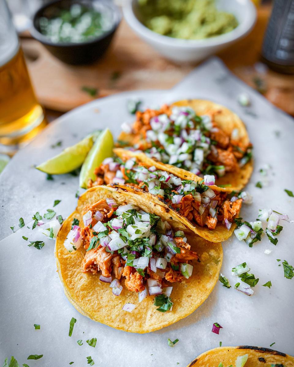 Close-up of three delicious Chicken Street Tacos topped with diced white onion, cilantro, and lime wedges.