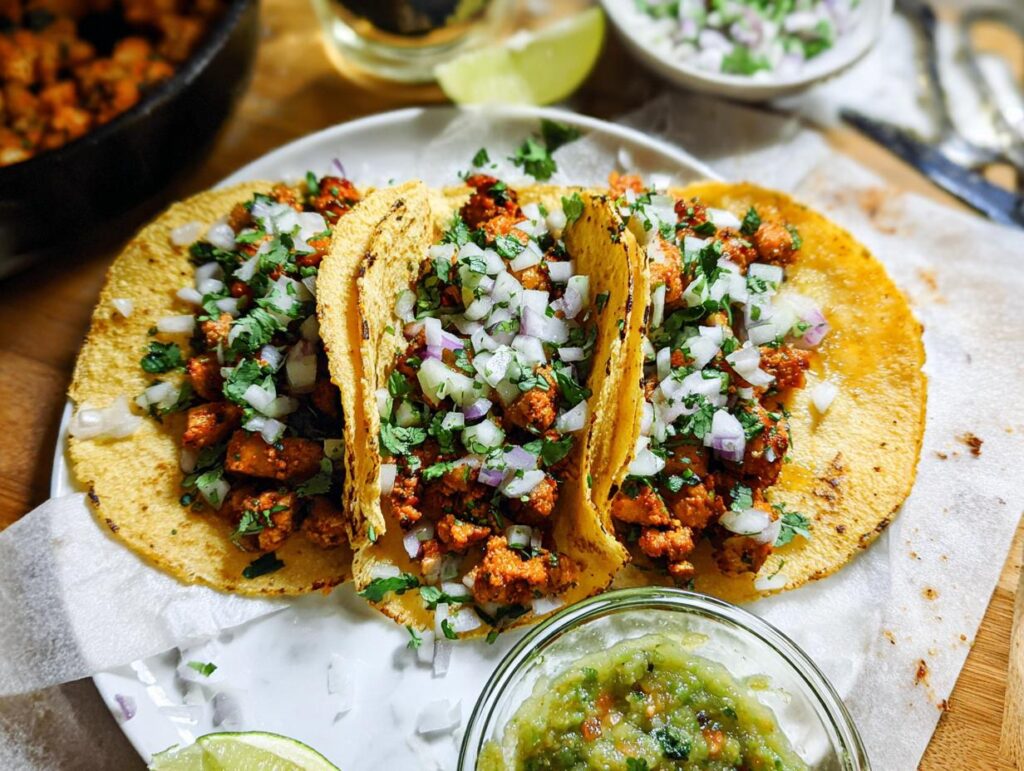 Three freshly made Chicken Street Tacos served on a white plate, topped with diced white onion and cilantro.