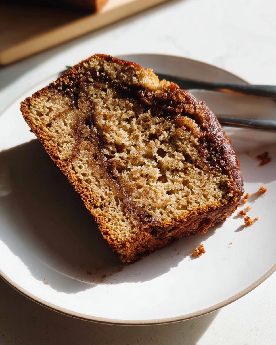 Close-up of a moist slice of Cinnamon Swirl Banana Bread on a white plate, showing the rich brown cinnamon swirl inside.