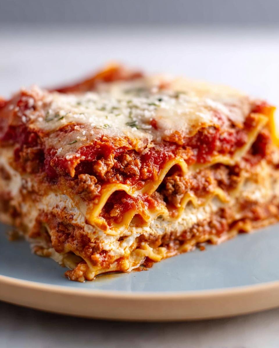 A close-up of a rich, layered slice of Classic Meat and Cheese Baked Lasagna on a blue plate.