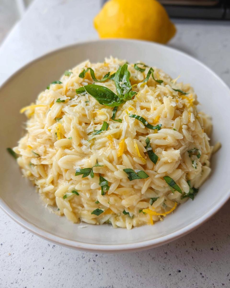 A close-up of creamy Lemon Parmesan Orzo topped with fresh basil, lemon zest, and grated cheese in a light bowl.