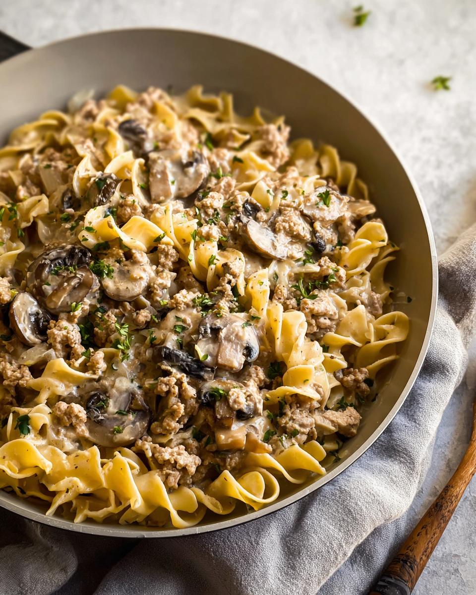 A close-up overhead view of Creamy Turkey Stroganoff mixed with egg noodles and sliced mushrooms in a skillet.