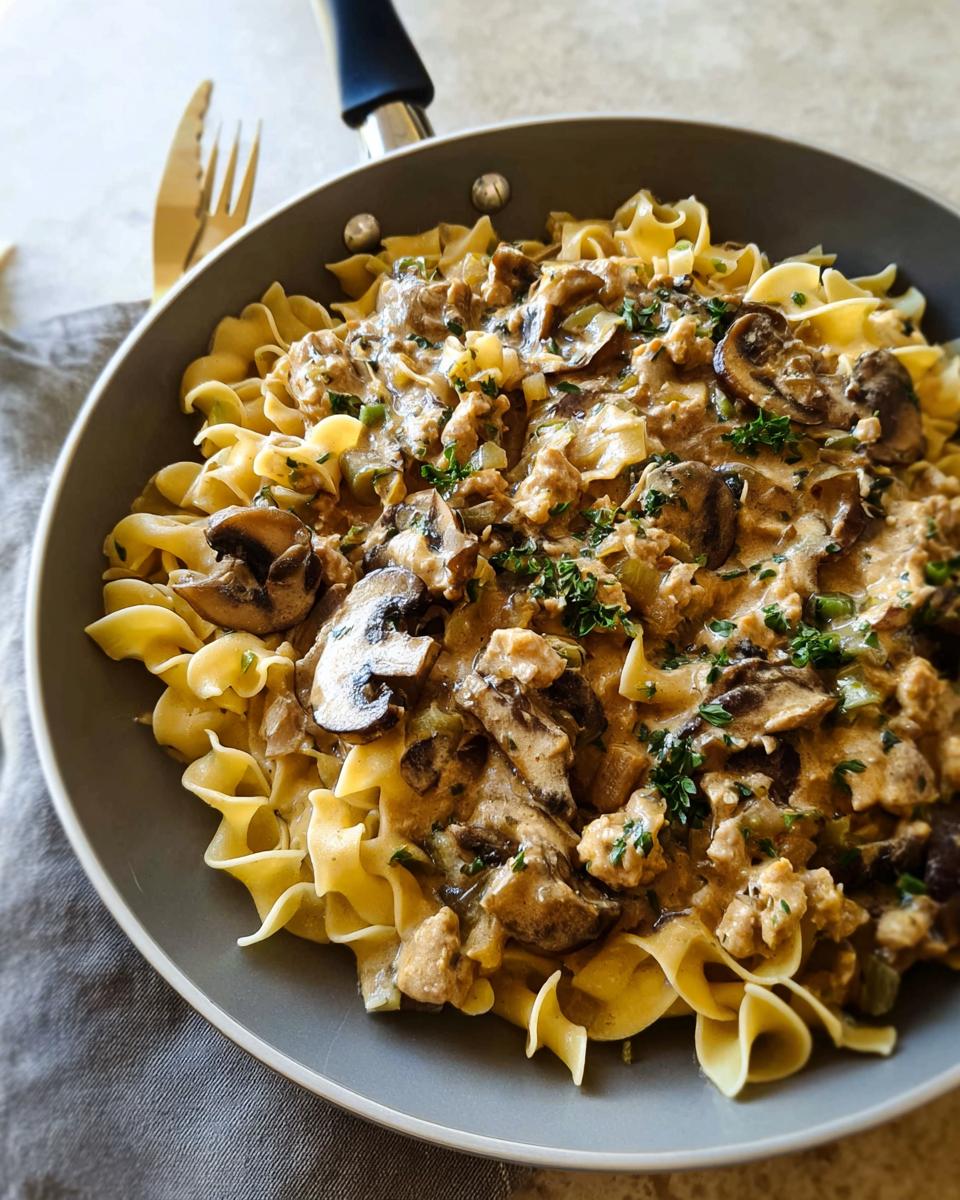 A skillet filled with Creamy Turkey Stroganoff served over wide egg noodles, topped with mushrooms and parsley.