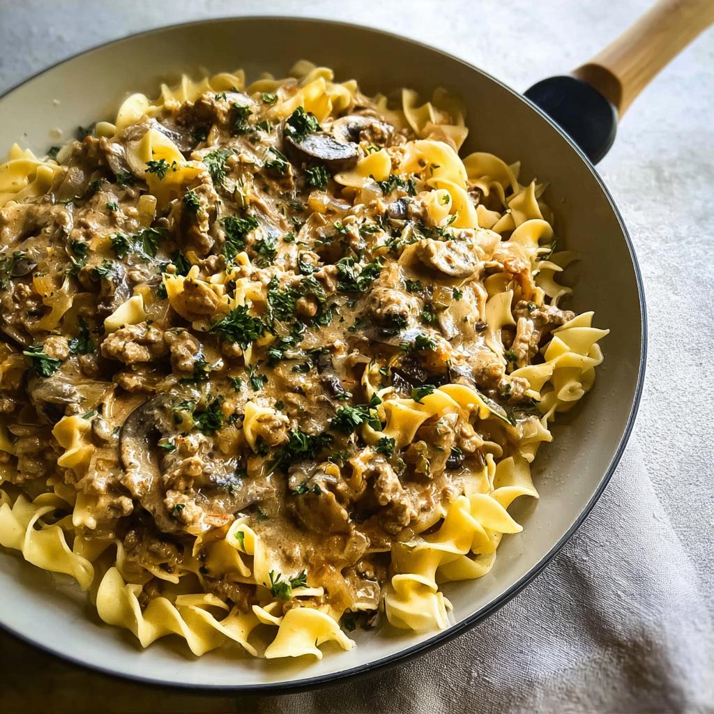A skillet filled with Creamy Turkey Stroganoff served over wide egg noodles and garnished with fresh parsley.