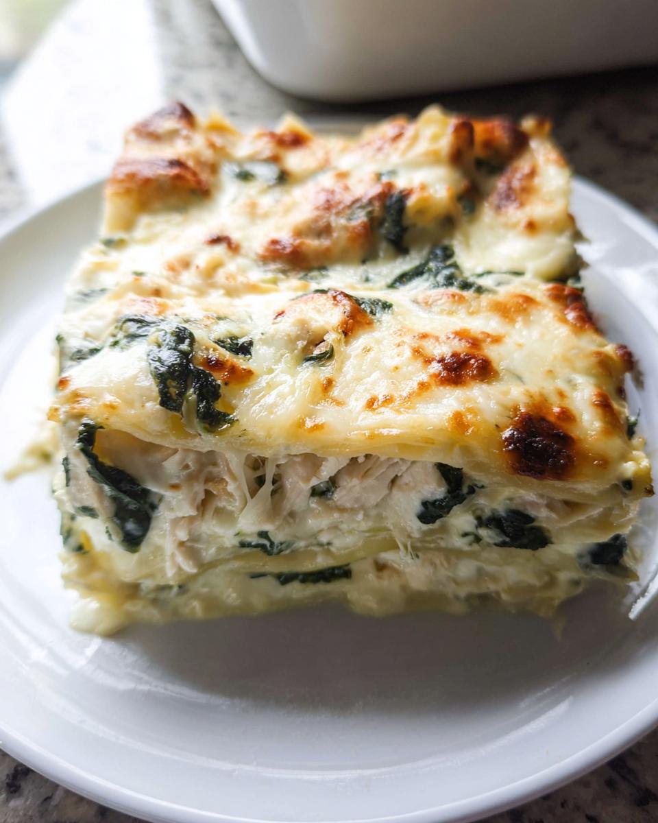 A close-up of a generous slice of Creamy White Chicken Spinach Lasagna on a white plate.