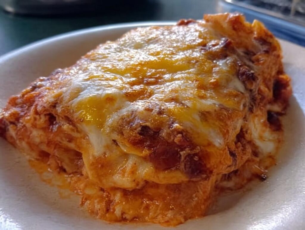 A close-up of a generous slice of Extra Cheesy Four Cheese Lasagna with a bubbly, golden-brown cheese topping.