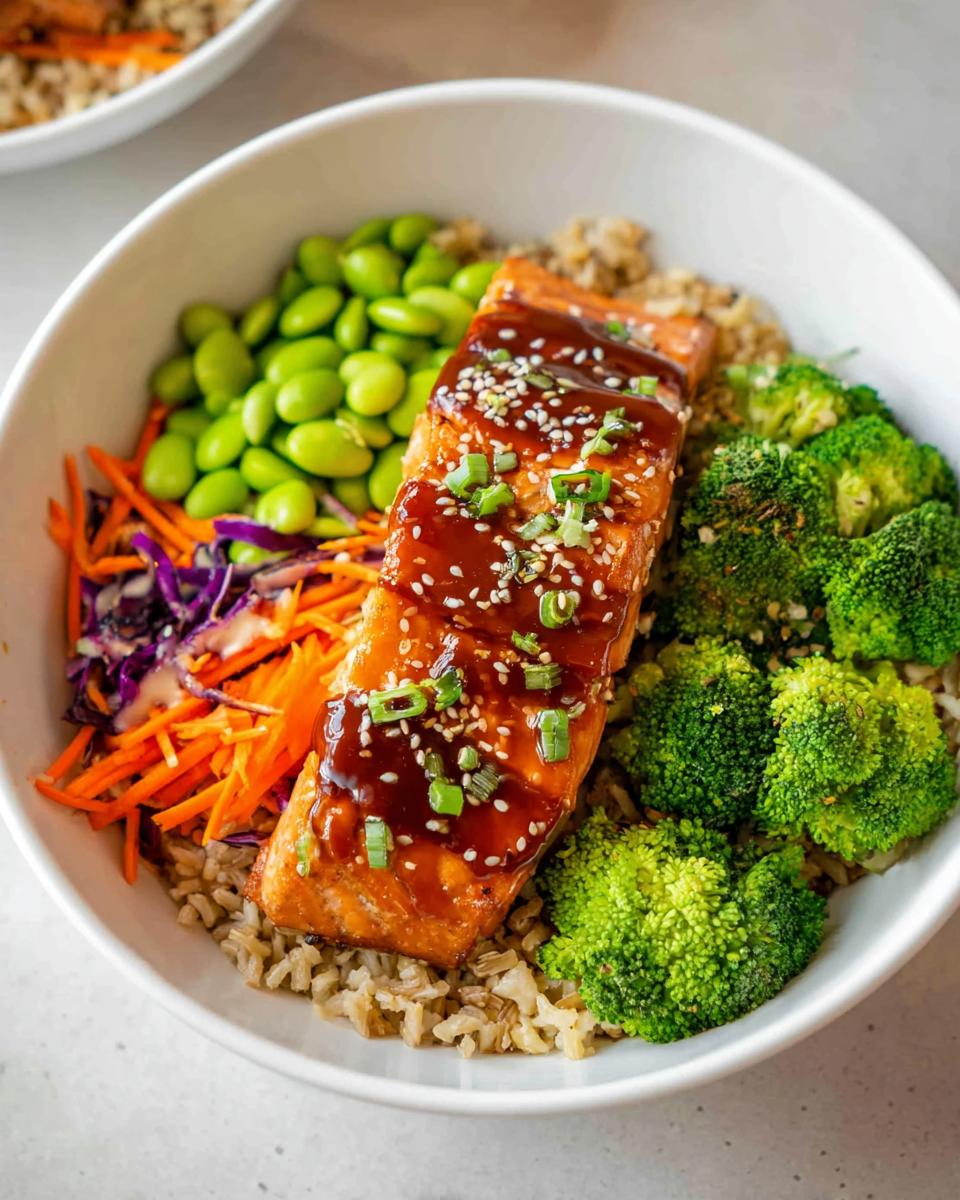 A close-up of a Healthy Teriyaki Salmon and Broccoli Bowl featuring glazed salmon over brown rice with edamame and shredded carrots.