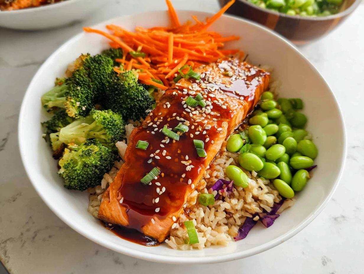 Close-up of a Healthy Teriyaki Salmon and Broccoli Bowl featuring glazed salmon over brown rice with edamame and shredded carrots.