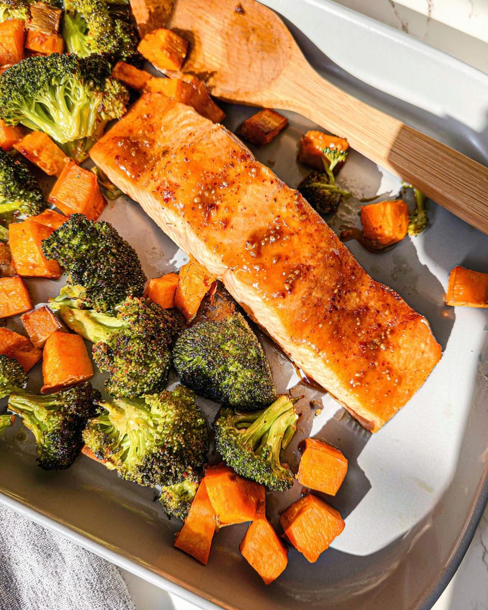 A close-up of a glazed salmon fillet surrounded by roasted broccoli and sweet potatoes in a sheet pan for the Maple Dijon Salmon Sheet Pan Dinner.