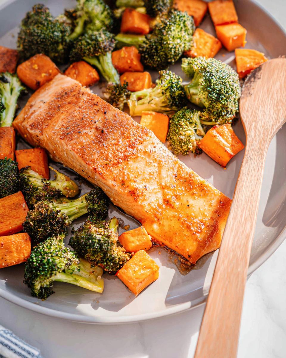 A perfectly cooked fillet of Maple Dijon Salmon Sheet Pan Dinner surrounded by roasted broccoli and diced sweet potatoes.
