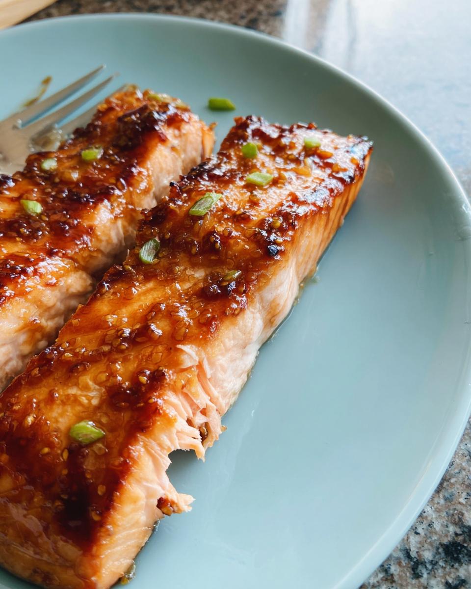 Two perfectly cooked fillets of Miso Glazed Broiled Salmon on a light blue plate, topped with sesame seeds and green onions.