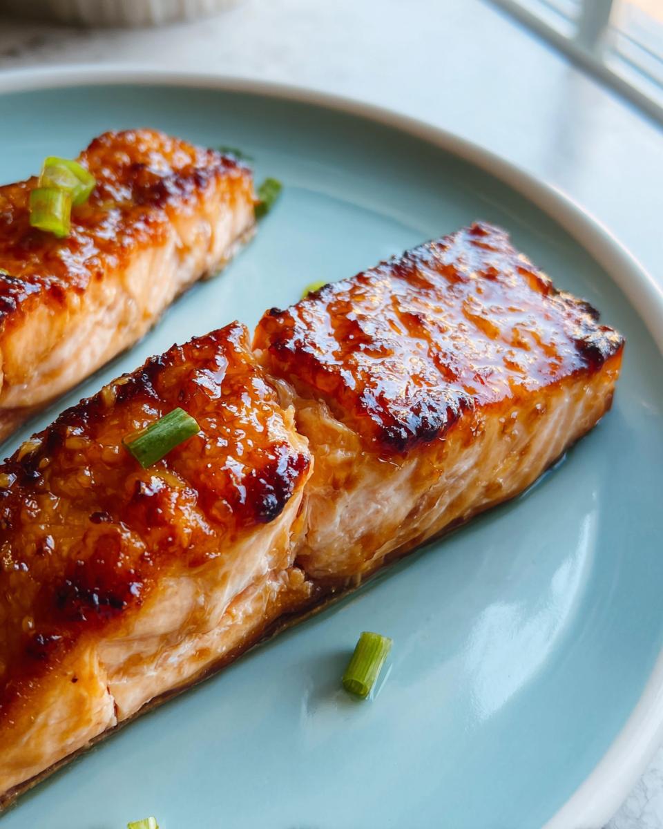 Two glistening fillets of Miso Glazed Broiled Salmon topped with chopped green onions on a light blue plate.