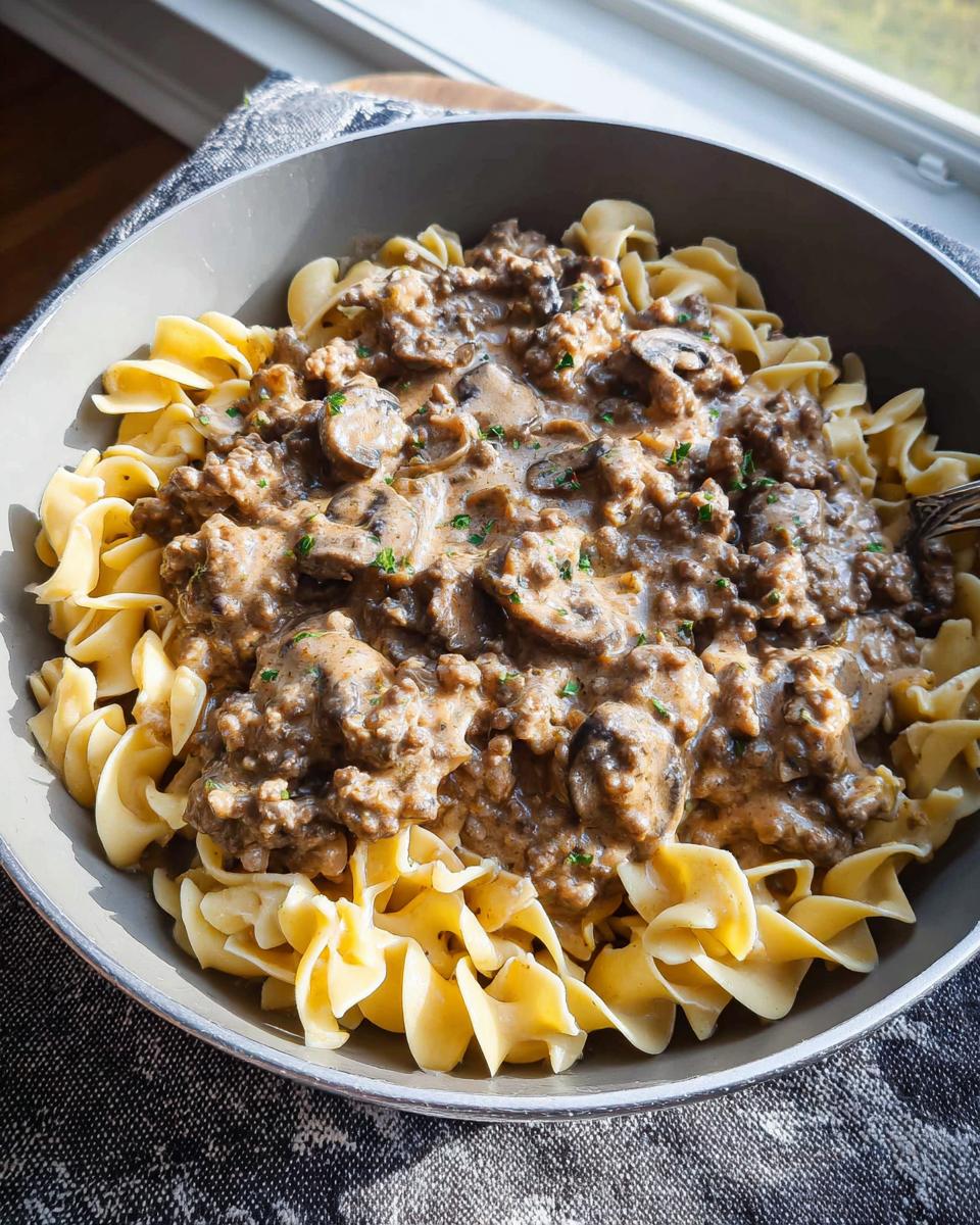 A close-up bowl of One Pot Ground Beef Stroganoff served over wide egg noodles, topped with mushrooms and parsley.