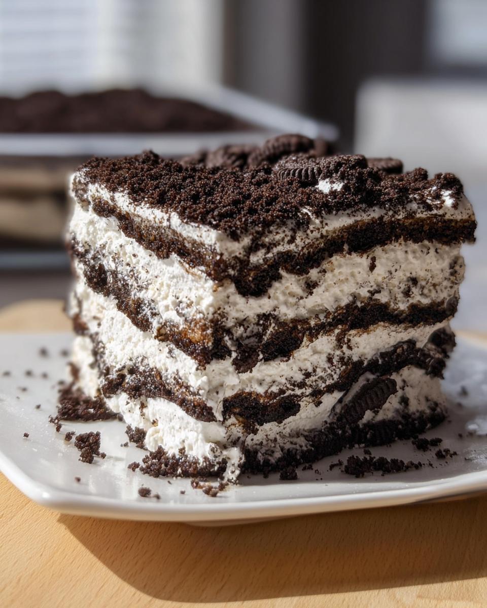 A tall, layered slice of Oreo Cookies and Cream Icebox Cake with whipped cream and crushed cookies.
