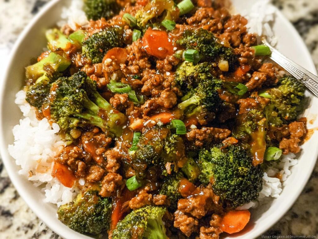 A close-up of a Teriyaki Ground Turkey Bowl featuring ground meat, bright green broccoli florets, carrots, and white rice, topped with green onions.