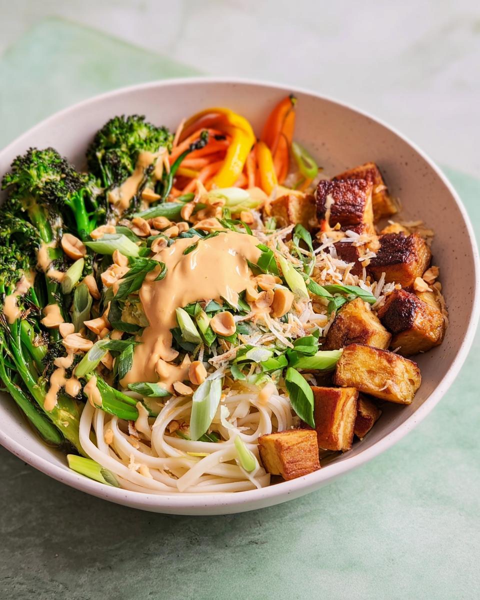 A close-up of a vibrant 20-Ingredient Rice Bowl with noodles, broccoli, carrots, crispy tofu, and a creamy peanut sauce.