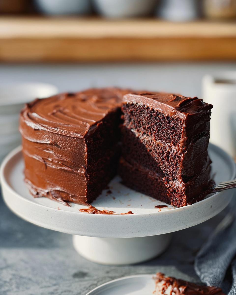 A decadent chocolate cake with rich frosting, a slice removed, showcasing its moist layers. Perfect for 7-Ingredient Cake Ideas.
