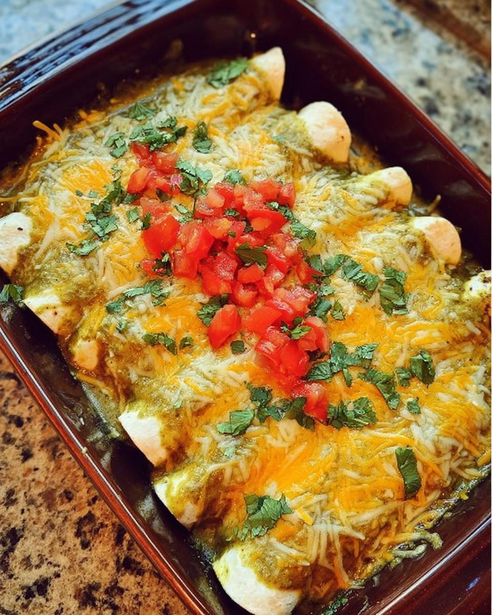 Close-up of baked chicken enchiladas topped with green sauce, melted cheese, diced tomatoes, and cilantro.